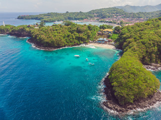Sea bay with turquoise water and a small white beach. Beautiful lagoon and volcanic island covered with dense forest, view from above