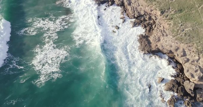 NATURE 4K Aerial forward motion tracking waves crashing on rocks with a dirth path following alongside the shore