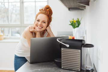 lächelnde frau steht in ihrer küche mit ihrem laptop