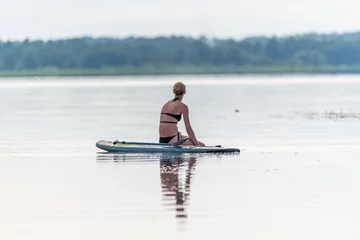 Foto op Canvas Female Paddler Sitting on a Stand Up Paddle Board on a Still Lake © JonShore
