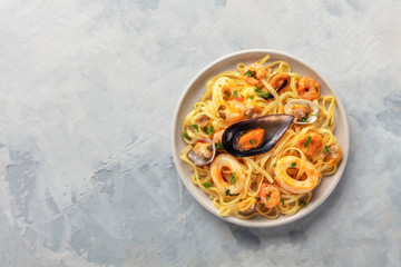 Seafood pasta. A plate of tagliolini with mussels, shrimps, clams and squids, shot from the top on a gray background with a place for text