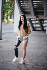 Photo of atlethic disabled woman in sportswear with prosthetic leg standing at the stairs and looking aside outdoor