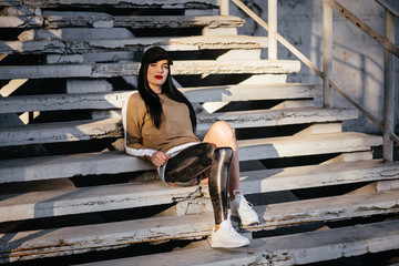 Portrait of attractive handicapped woman in black tracksuit with prosthetic leg sitting at the...