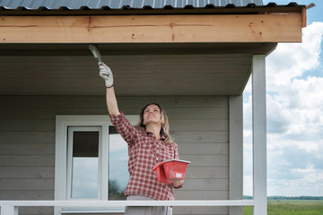young European woman painting the veranda of a new wooden house