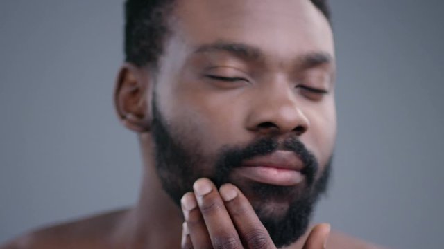 Close-up of attractive black topless gentleman looking at camera. Portrait of young man touching his black beard before shaving in the bathroom.