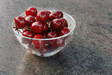 ripe red sweet cherry in a glass container on the table in the rays of the setting sun