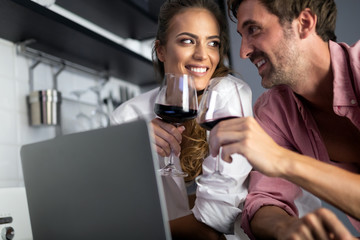 Young couple relaxing in kitchen with wine and laptop. Love, technology, people concept.
