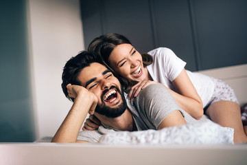 Beautiful couple is smiling and hugging while spending time together in bedroom