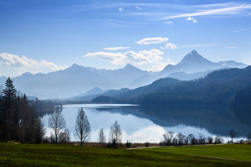 Fototapeta na wymiar weissensee lake in morning light in front of the mountains of the bavarian alps against a blue sky near fuessen, allgaeu, southern germany, copy space