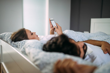 Young woman texting someone while boyfriend is asleep