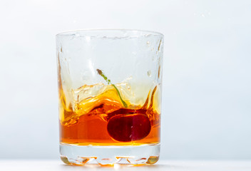 ripe red cherry fell with a splash in a glass of liquor close-up on a white background