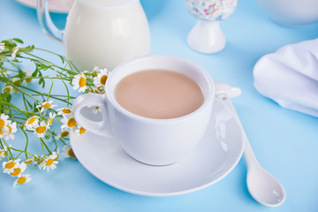 Morning. Breakfast. Cup of tea with milk, jar with milk, egg on the blue background