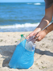 Man picking bottles into garbigde bag. Cleaning the beach in the morning time, Volunteer concept. Plastic pollution of the environment. Cleaning the beach from trash. Vertical shot