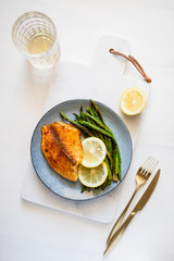 Roasted tilapia fish with asparagus on a ceramic plate. Healthy mediterranean diet lunch or dinner. Top view, flat lay.