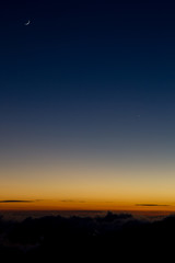Crescent moon over the bright orange horizon lit by the last light of sunset at the Mauna Kea on Big Island, Hawaii, USA.