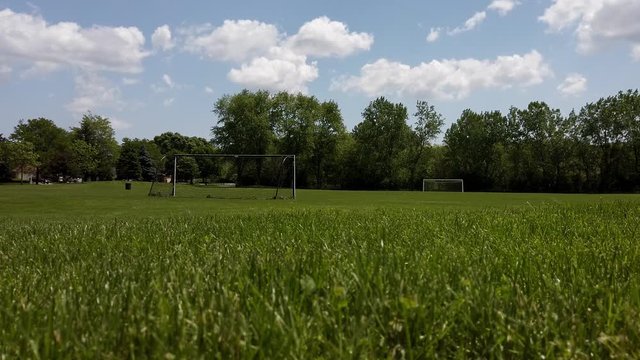Beautiful day, a bright blue sky with some puffy clouds crossing. A soccer field in a quite park in 4K.