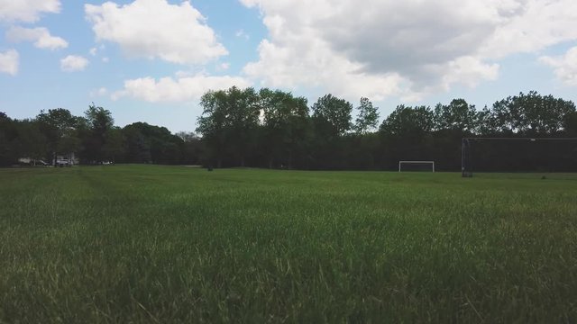 Beautiful day, a bright blue sky with some puffy clouds crossing. A soccer field in a quite park in 4K.