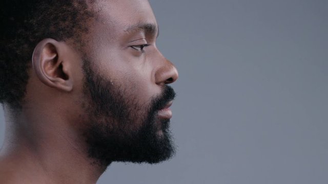 Profile of attractive topless emotionless afro-american young man standing straight looking forward isolated on dark background.