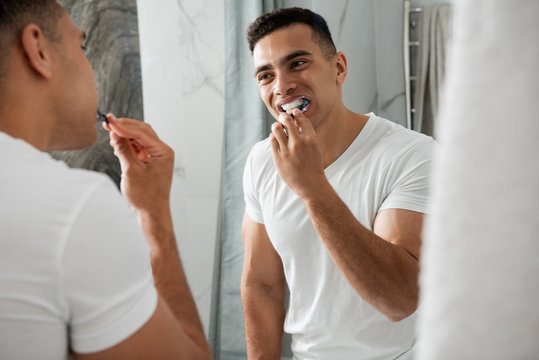 Back side of young smiling man brushing teeth