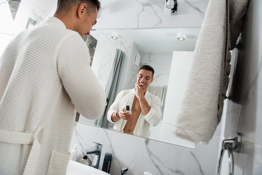 Young happy man with cologne bottle in bathroom - Powered by Adobe