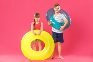 Cute little children with inflatable rings on color background