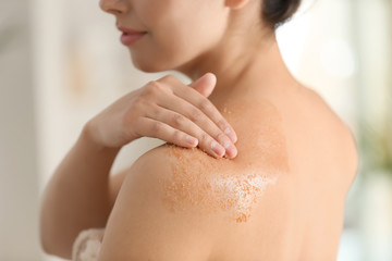 Beautiful young woman applying body scrub at home, closeup