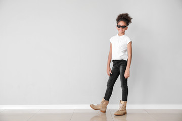 Stylish African-American girl in jeans near light wall