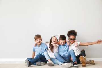 Happy children in jeans sitting near light wall