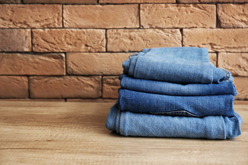 Stack of jeans clothes on table against brick wall