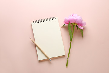 Beautiful fresh peony flower and notebook on color background