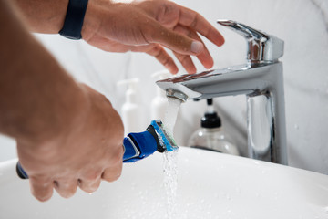 Young man washing razor under tap water