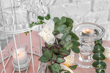 Decorative cage, burning candles and eucalyptus branches on table