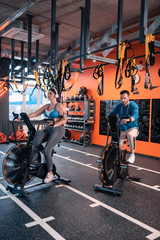 Athletic trainer cycling in gym nearby his overweight client