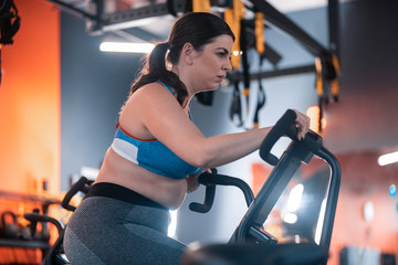Plump woman cycling in gym feeling truly exhausted