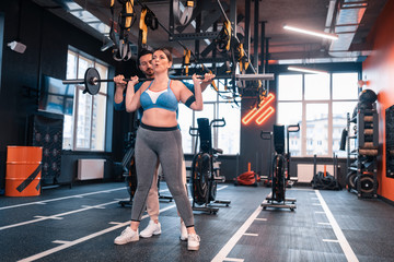 Fototapeta na wymiar Woman hardly breathing after lifting barbell standing near trainer