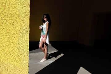 Pretty girl with cup of coffee standing in underpass with yellow walls