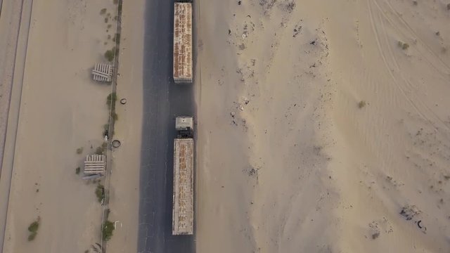 Fly backwards over a long line of trucks in the desert over a cracked road (4K)