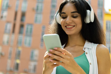 Beautiful brunette girl in wireless headphones holding white cellphone