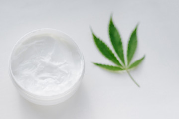 Open jar of hemp cream with cannabis leaf on white isolated background. Top view with moisturizing lotion from natural products containing CBD. Flat composition with marijuana and copy space