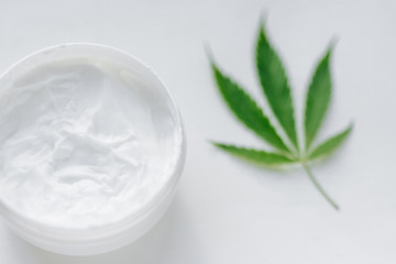 Top view jar of hemp cream with cannabis green leaf on white background. Moisturizing lotion from natural products containing CBD