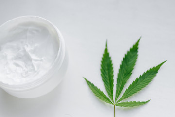 Open jar of hemp cream with cannabis leaf on white isolated background. Top view with moisturizing lotion from natural products containing CBD. Flat composition with marijuana and copy space