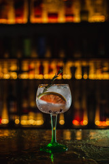 A vertical photo of a refreshing gin&tonic cocktail in a bar, with a slice of grapefruit and rosemary.