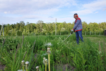 The headphone and glasses worker mows the grass in the field.