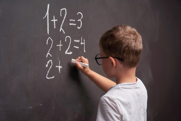 Rear view of a schoolboy solves a mathematical example on a blackboard in a math class.