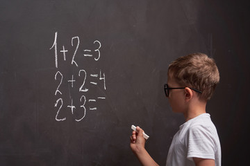 Primary education. Rear view of a schoolboy solves a mathematical example on a blackboard in a math class.