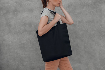 Young woman with black cotton bag in her hands on grey background. Mock up.