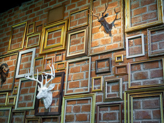Various empty photo frames with plaster deer head hanging on brick wall