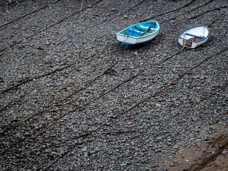 Two rowing boats lying on top of chains on a pebble beach