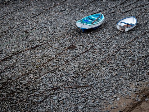 Two rowing boats lying on top of chains on a pebble beach - Powered by Adobe