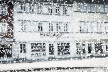 First snow and snowflakes on a window glass on the blurred house background